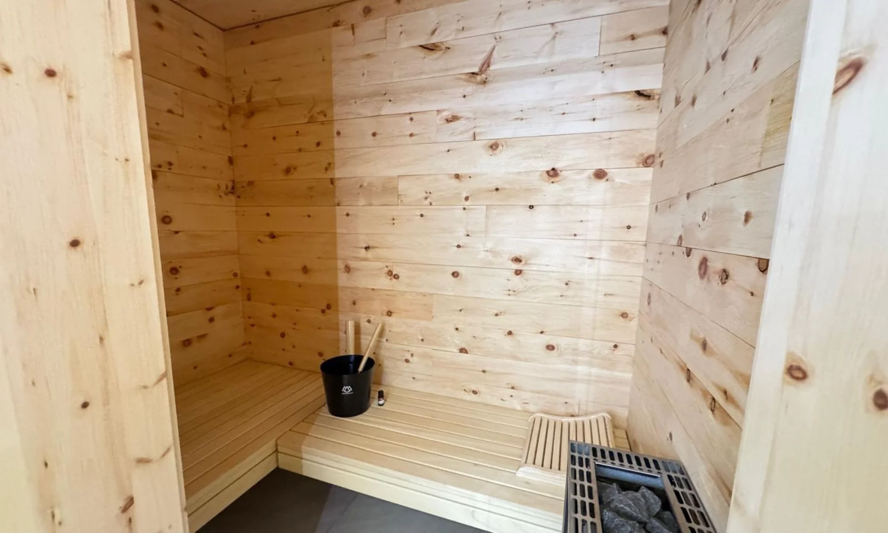 Private Zirbensauna mit hellem Holz, Sitzbank, Saunaeimer und Ofen in der Alpenherz Suite