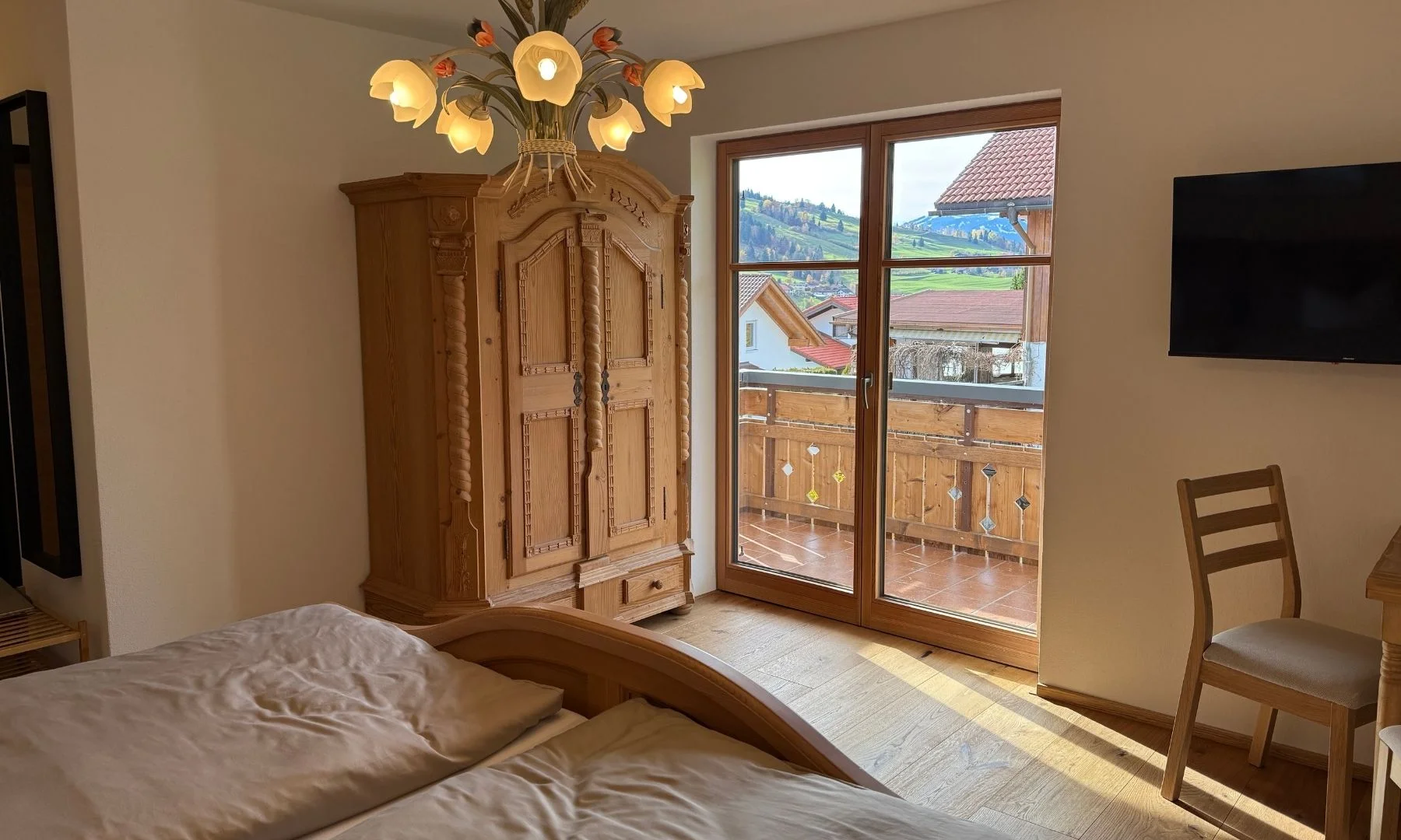Wohn-Schlafbereich mit rustikalem Holzschrank, Doppelbett und Balkontür mit Bergblick